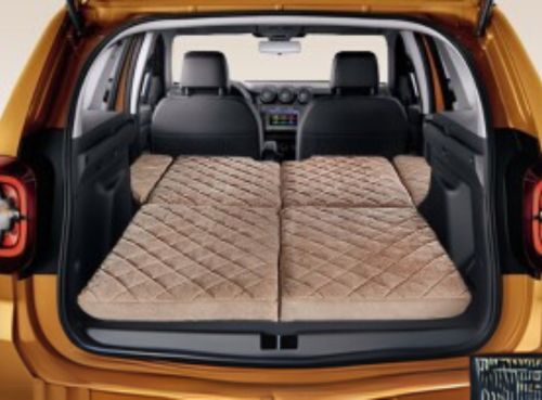 Rear view of a car with the back seats folded down and covered by a beige quilted mattress, creating a flat sleeping or resting area.
