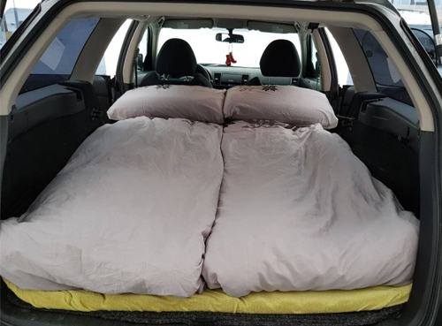 The back of a car with its seats folded down, fitted with a mattress and bedding to create a sleeping area.